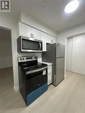Waterloo apartment for rent - A stainless steel refrigerator stands in a kitchen with white cabinets and a microwave above the oven.