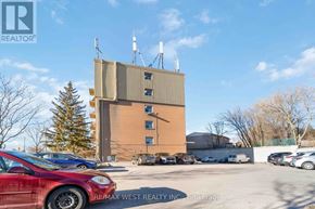 Kitchener condo for rent - A parking lot with a red car in the foreground and a multi-story building in the background.