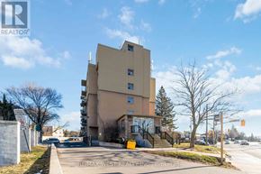 Kitchener condo for rent - A building with a beige and brown facade is surrounded by a grassy area and a sidewalk.