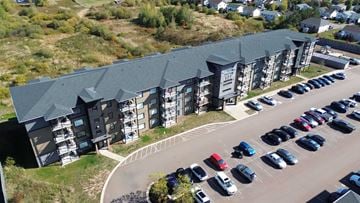 Moncton apartment for rent - A parking lot with cars and a building with a green roof.