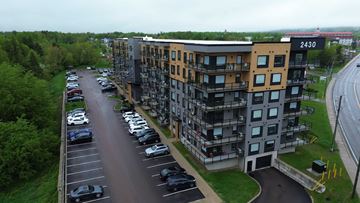 Moncton apartment for rent - A parking lot with cars parked in front of a multi-story building with the number 2430 on it.