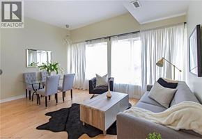 Hamilton apartment for rent - A living room with a grey couch, a coffee table, a dining table with chairs, and a large window with curtains.