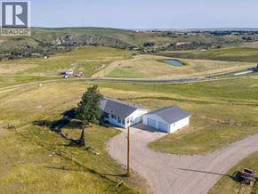 For rent in Rural Cardston County - A house with a driveway in the foreground and a grassy field in the background.
