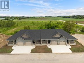 Huron East (Seaforth) townhouse for rent - A large, two-story house with a grey roof and a white garage door is surrounded by a grassy field.