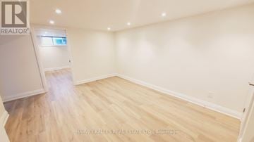 Toronto (Englemount-Lawrence) duplex for rent - A spacious room with wooden flooring and white walls, featuring a kitchen area with cabinets and a window.