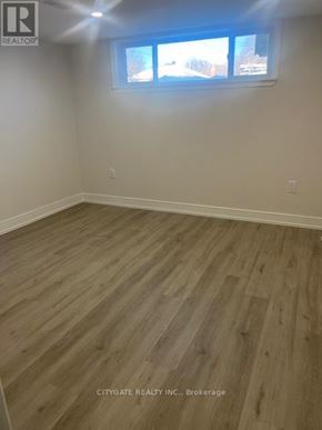 Toronto (Cliffcrest) house for rent - A room with wooden flooring and a window showing a view of trees and houses outside.