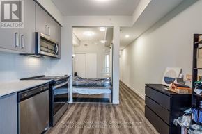 Hamilton (Central) condo for rent - A kitchen area with a dishwasher, microwave, and a bed in the background.