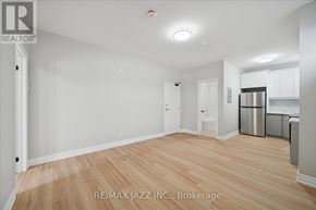 Oshawa (Central) multi-family for rent - A spacious room with wooden flooring and white walls, with a kitchen area visible in the background.