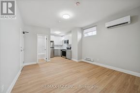 Oshawa (Central) multi-family for rent - A spacious room with wooden flooring and a kitchen area in the background.