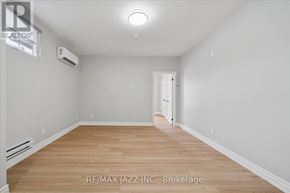 Oshawa (Central) multi-family for rent - A spacious room with wooden flooring and white walls, featuring a brokerage sign.