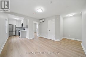 Oshawa (Central) multi-family for rent - A spacious room with wooden flooring and white walls, featuring a kitchenette with stainless steel appliances.