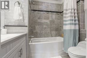 Hamilton house for rent - A bathroom with a white tub and toilet, a shower with a striped shower curtain, and a towel hanging on the wall.