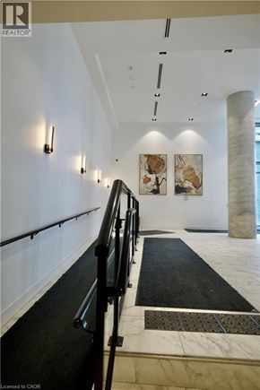 Kitchener condo for rent - A hallway with a black and white carpet, a black railing and a white wall with a painting on it.