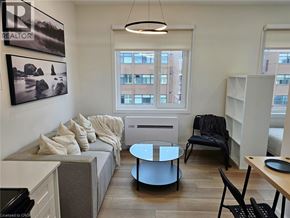 St. Catharines apartment for rent - A living room with a grey couch, a black chair, and a round glass table.