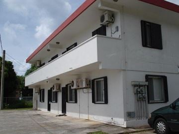 Hagatna apartment for rent - A white building with a red roof and a black van parked in front.