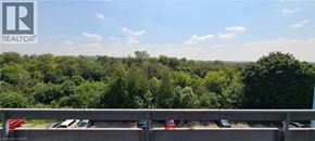 Guelph condo for rent - A parking lot with cars and a view of a wooded area.