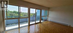 Guelph condo for rent - A large empty room with a view of trees through the windows.