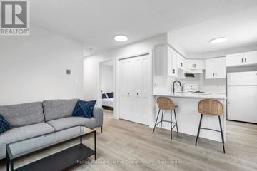 Kitchener fourplex for rent - A modern living room with a grey couch and a kitchen area in the background.