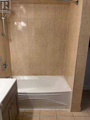 St. Catharines (Downtown) duplex for rent - A white bathtub in a bathroom with beige tiled walls.