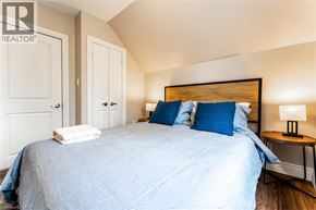 Stratford apartment for rent - A bedroom with a bed, two pillows, a nightstand with a lamp, and a wall-mounted light fixture.