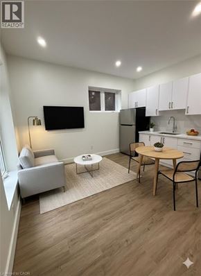 Hamilton apartment for rent - A living room with a grey couch, a white chair, a wooden table, and a television mounted on the wall.