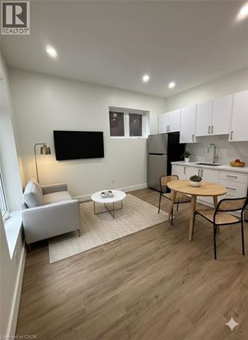 Hamilton apartment for rent - A living room with a grey couch, a white chair, a wooden table, and a television mounted on the wall.