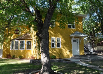 Saskatoon apartment for rent - A yellow house with a tree in front.