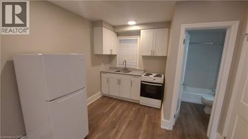 Kitchener apartment for rent - A small kitchen with a refrigerator, cabinets, and a stove top oven.