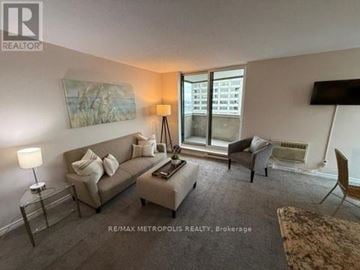 Sarnia condo for rent - A living room with a grey couch, a white chair, and a painting on the wall.