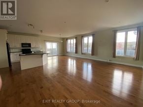 Quinte West (Murray Ward) apartment for rent - A spacious room with wooden flooring and a kitchen area with white cabinets.