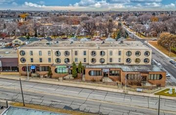 Edmonton apartment for rent - A large building with a green sign on the front is surrounded by trees and other buildings.