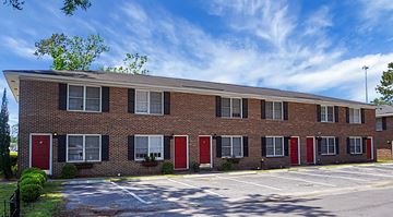 Summerville apartment for rent - A long brick building with red doors and windows.