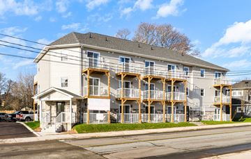Moncton apartment for rent - A two-story apartment building with balconies and a parking lot in front.