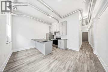 Brantford apartment for rent - A spacious kitchen with a sink, stove, and cabinets in a white room with wood flooring and exposed pipes.