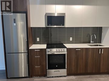 Toronto (Weston-Pellam Park) condo for rent - A modern kitchen with a stainless steel refrigerator, a microwave above the stove, and wooden cabinets.