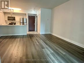 Ottawa condo for rent - A room with a wooden floor and a kitchenette in the background.
