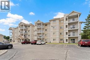 Windsor condo for rent - A large apartment complex with a parking lot in front.