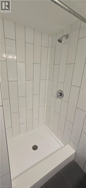 Kitchener apartment for rent - A white tiled shower with a drain in the middle.