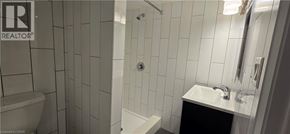 Kitchener apartment for rent - A white tiled bathroom with a toilet, sink, and bathtub.