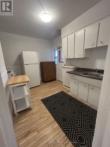 Toronto (South Parkdale) multi-family for rent - A kitchen with white cabinets and a black and white rug on the floor.