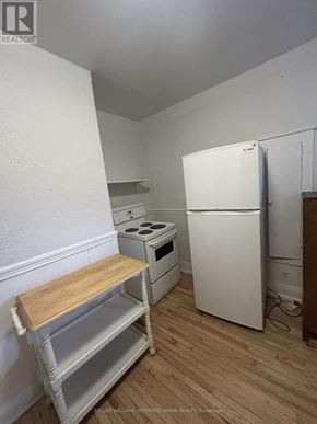 Toronto (South Parkdale) multi-family for rent - A kitchen with a white fridge, stove and a wooden table.
