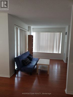 Toronto (Bay Street Corridor) condo for rent - A blue couch with two pillows sits in a room with a window and a wooden floor.
