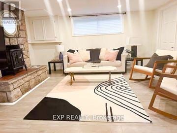 Cobourg apartment for rent - A living room with a white couch, a stone fireplace, and a rug with black lines.