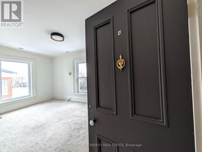 Prince Edward County (Picton Ward) fourplex for rent - A black door with a brass handle is in the foreground of a room with a carpeted floor and a window.