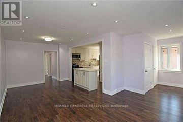 Brampton (Brampton South) apartment for rent - A spacious room with wooden floors and white walls, featuring a kitchen area with a sink and cabinets.
