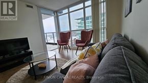 Toronto (Bayview Village) condo for rent - A living room with a grey couch, a glass table, and a television.