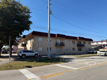 Hialeah apartment for rent - A white car is parked in front of a building with a red roof.