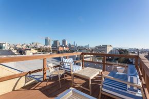 San Francisco apartment for rent - A balcony with striped chairs and a table overlooking a city skyline.
