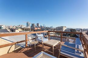 San Francisco apartment for rent - A balcony with striped chairs and a table overlooking a city skyline.