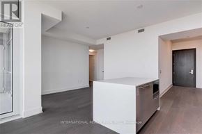 Toronto (Annex) condo for rent - A spacious, empty room with a kitchen area in the foreground.